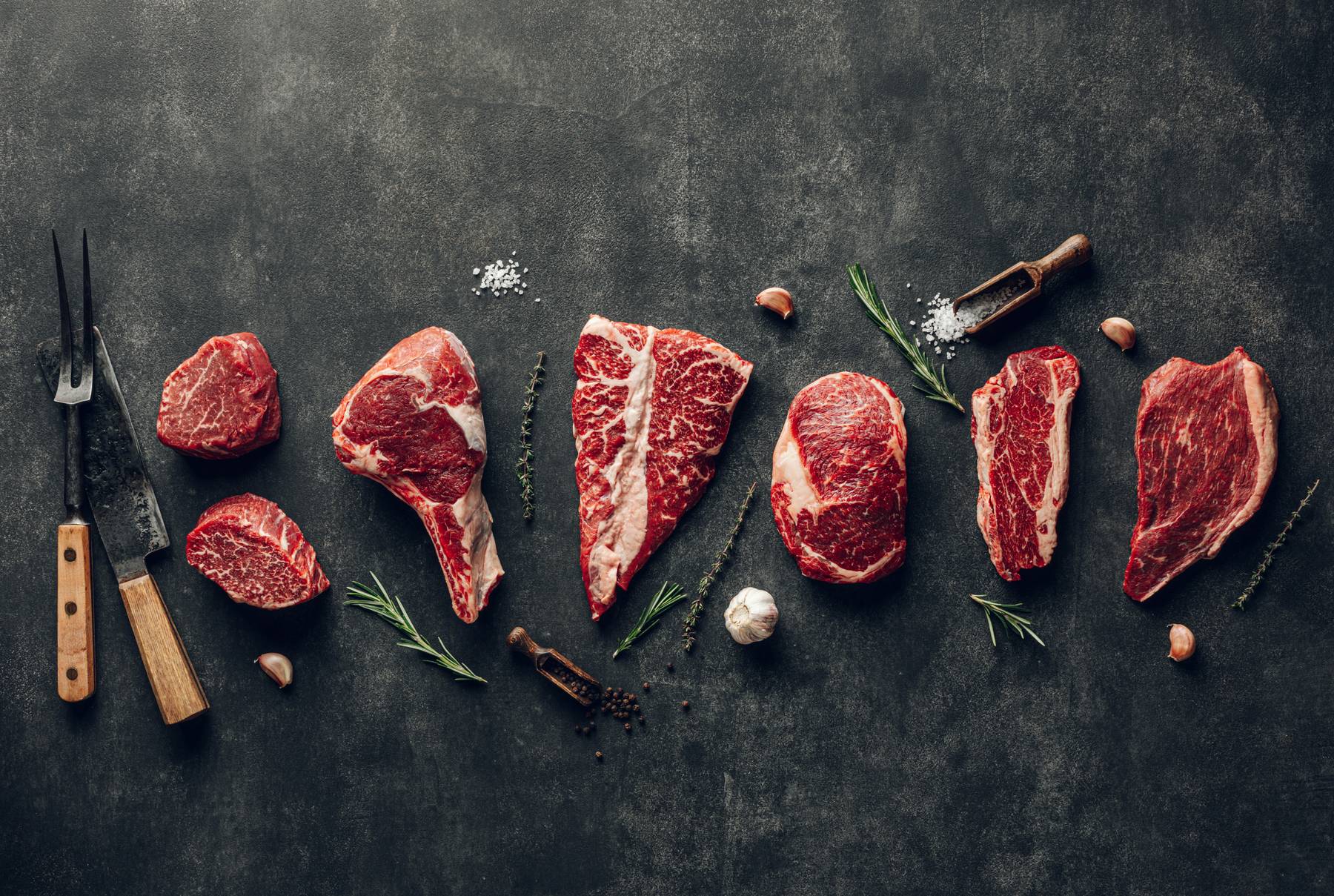 Raw prime steaks with rosemary, garlic and sea salt on dark slate