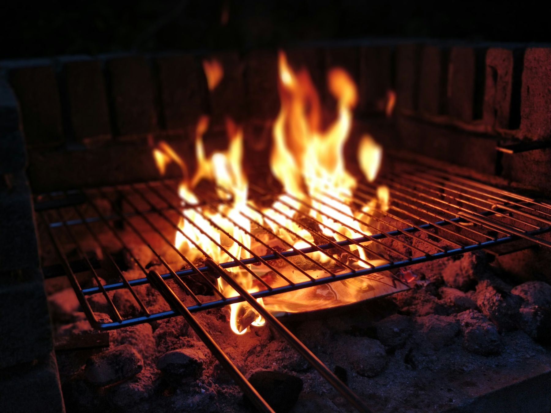 Flames rising through the grill grate over glowing coals